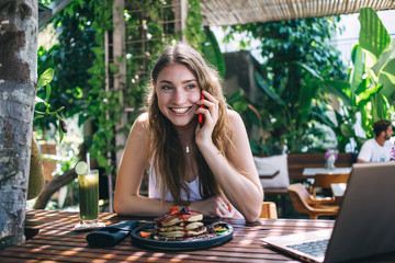 Happy young female talking on phone during breakfast