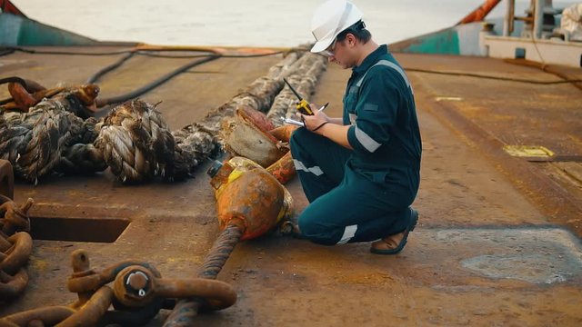 Marine chief officer or chief mate on deck of ship or vessel. He fills up ahts vessel checklist. Ship routine paperwork. He holds VHF walkie-talkie radio in hands.