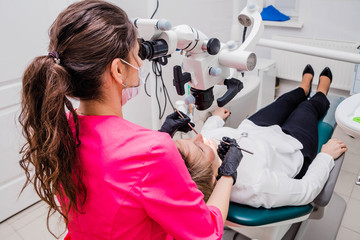 A female professional dentist examines a female patient with a stamotologic microscope in her office. Stamotologist profession concept