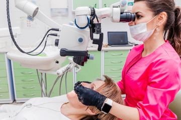 A female professional dentist examines a female patient with a stamotologic microscope in her office. Stamotologist profession concept