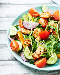 Healthy Salad with Chicken Briest, Cherry Tomatoes, Cucumber, Rocket and fresh Basil. Bright wooden background.