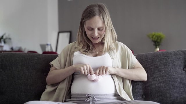 Front view of pregnant woman playing with babys bootees on belly. Smiling future mother talking with child. Pregnancy concept
