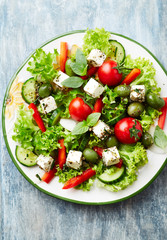  Healthy salad with feta chesse, green olives, cherry tomatoes, red pepper, lettuce and fresh herbs. Wooden background. Top view.
