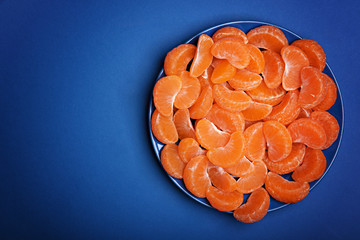 Many peeled mandarin slices on the blue plate. Classic blue background. Color of the year 2020, Classic Blue.
