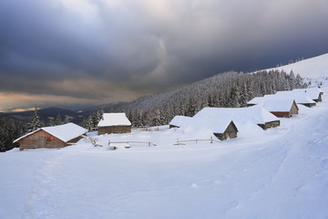 Fototapeta na wymiar Majestic winter scenery. Dramatic sky. Old wooden huts on the lawn covered with snow. Landscape of high mountains and forests. Wallpaper background. Location place Carpathian, Ukraine, Europe.