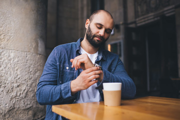 Young modern man checking time while having drink in cafe