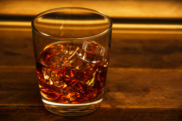 Whiskey with ice or brandy in a glass and a square carafe on an old wooden background. Whiskey with ice in a glass. Whiskey or cognac. Selective focus.
