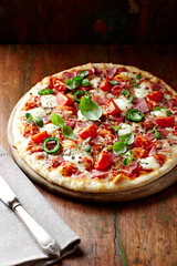 Pizza with ham, cherry tomatoes, mozzarella cheese, jalapeno pepper and fresh herbs. Rustic wooden background.