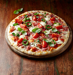 Pizza with ham, cherry tomatoes, mozzarella cheese, jalapeno pepper and fresh herbs. Rustic wooden background. 