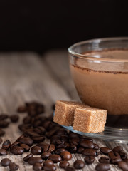 Glass cup with coffee with milk, latte coffee. Cane sugar on a saucer. Coffee beans on a wooden background. Close-up. Vertical orientation.