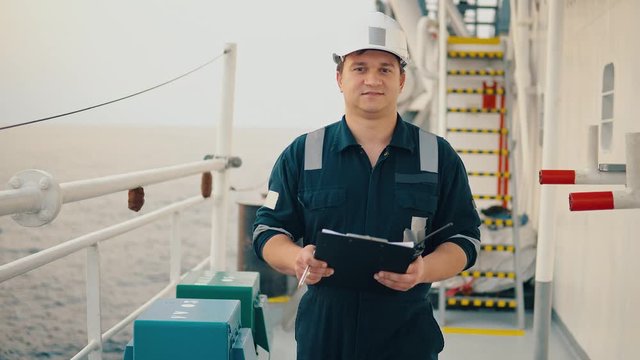 Marine chief officer or chief mate on deck of ship or vessel. He fills up ahts vessel checklist. Ship routine paperwork. He holds VHF walkie-talkie radio in hands.