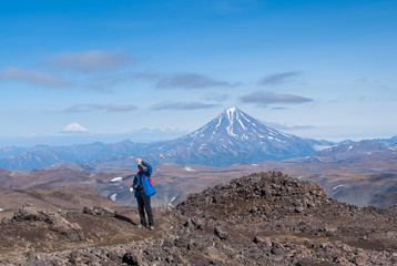 young man traveler photographer at the top of the volcano mountain shows excellent, rejoices, volcanic view in the crater of the volcano, the traveler at the height, the view of the mountain tops