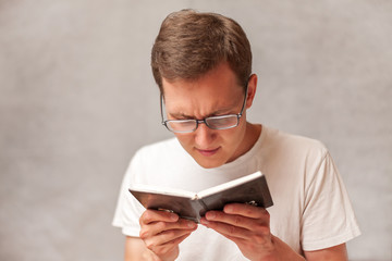 the young man holds glasses with diopter lenses and looking at the book, the problem of myopia,...