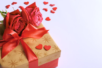 Golden gift box with red ribbon, roses and little hearts, concept of Valentine's day, anniversary, mother's day or birthday greeting, copy space, closeup view.
