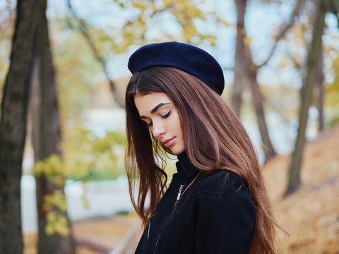 Headshot of young elegant french style brown haired woman in beret and black leather jacket enjoying free time strolling in fall city park cinematic stock colour grading