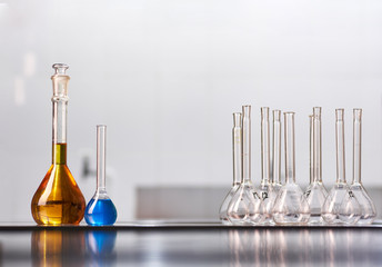 A set of jars and flasks with colored reagent solutions in a real laboratory. Large light empty space for text placement.