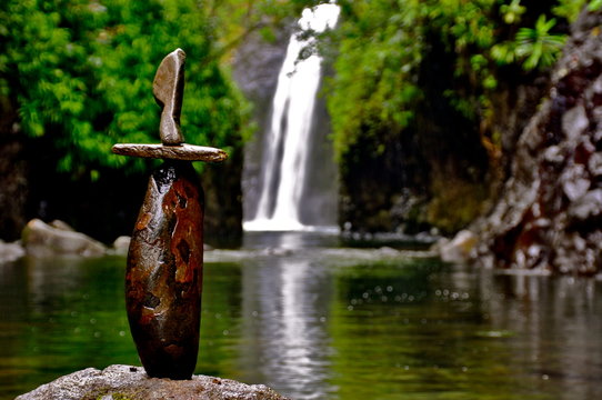 A delicately balanced rock cairn stands in front of a tropical waterfall 