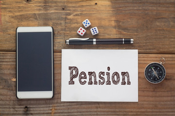 Pension Word written on white on wooden desk with dice,compass,smart phone and pen.Top view conceptual