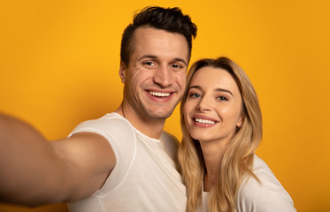 Obraz premium Looking into the bright future. Close-up photo of a young blonde girl and a dark-haired man, who are hugging while making a joint selfie.