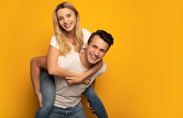 Having fun together. A handsome man is giving his blonde girlfriend a piggyback ride while laughing...