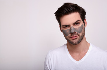 Portrait of a handsome guy in a white t-shirt in a cosmetic face mask.