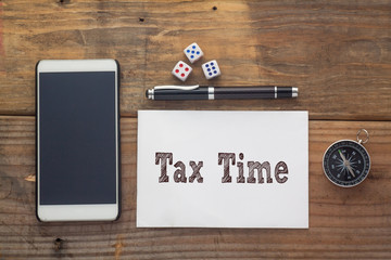 Tax Time Words written on white on wooden desk with dice,compass,smart phone and pen.Top view conceptual