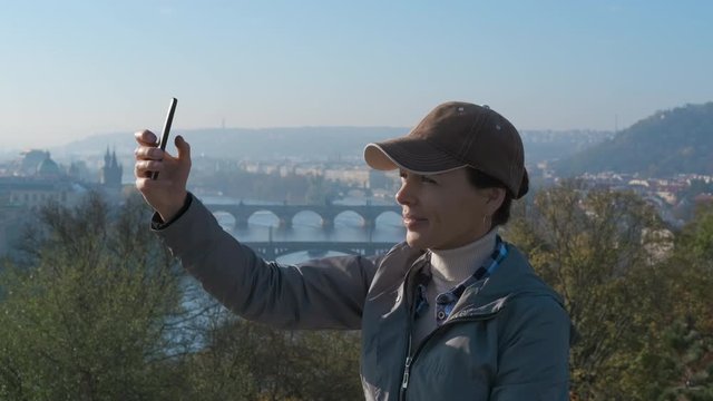 Selfie of a tourist. A cute girl tourist is photographed on a smartphone against the background of Prague bridges.