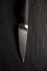 A small kitchen knife with a black handle on a dark Stone background. Scratched steel surface of...