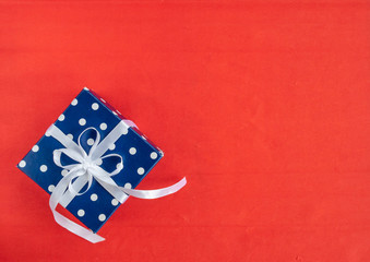 Blue polka dot gift box on red background. Birthday and Valentines day concept, top view, flat lay.