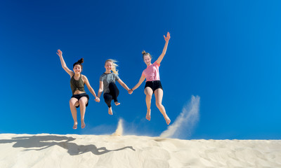3 Mädchen springen im Sommer voller Lebensfreude von einer Sanddüne und wirbeln dabei Staub auf