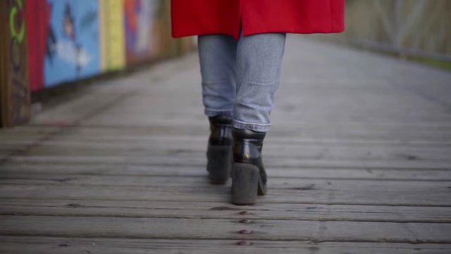 woman in boots on high wide heels walks along bridge closeup
