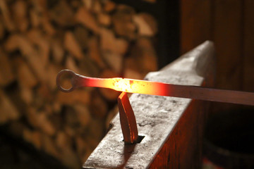 Ein Schmied bearbeitet mit seinem Hammer ein glühendes Stück Metall auf dem Amboss