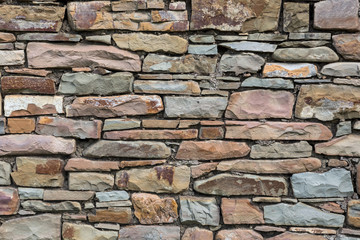 The wall is made of wild natural stone, warm colors. Background, texture.