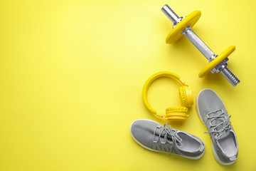 Dumbbell with shoes and headphones on color background
