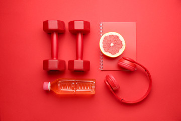 Dumbbells with notebook, headphones grapefruit and bottle of water on color background
