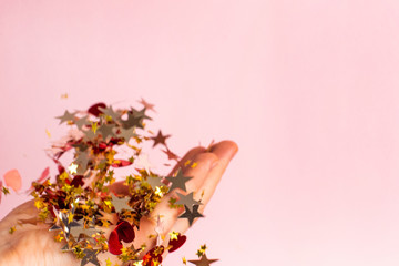 Gold and red confetti in women's hand on pastel pink background. Bright and festive holiday background.