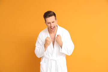 Happy man in bathrobe on color background