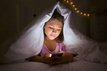 Teenage girl with mobile phone under blanket at night