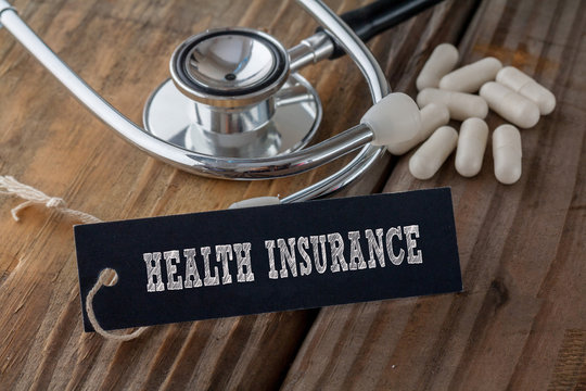 Health Insurance Written On Label Tag With Pills And Stethoscope On Wood Background