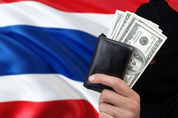 Thailand security and crime concept. Black criminals wear a head yarn, hold a dollar banknotes on national background.