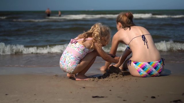 Family girls daughter and mom in swimsuits build wet sand castle on sea shore