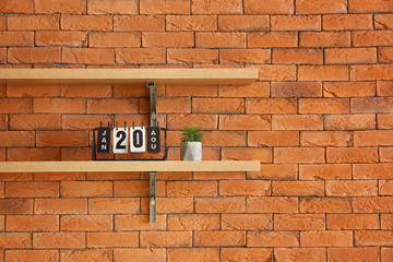 Fototapeta na wymiar Shelves with calendar and houseplant hanging on brick wall