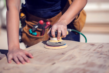 Young handy woman with short blond hair sanding wooden surface.