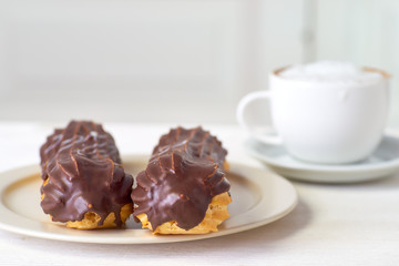 Two eclairs and cup of cappuccino on white wooden table