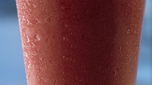 water droplet travels down on the exterior of a cold cup of strawberry slushy in extreme close up