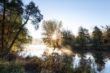Obraz premium Sonnenstern durch Bäume am See, Herbstfoto