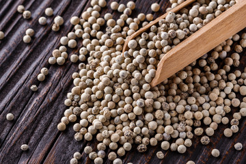 white peppercorns in wooden scoop on rustic background