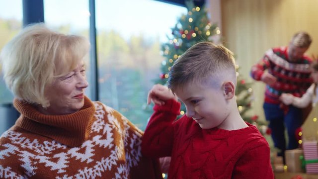 Happy grandmother and little kid celebrating family Christmas holidays at home. Surprised elderly woman receiving a present from grandson hugging tight together.
