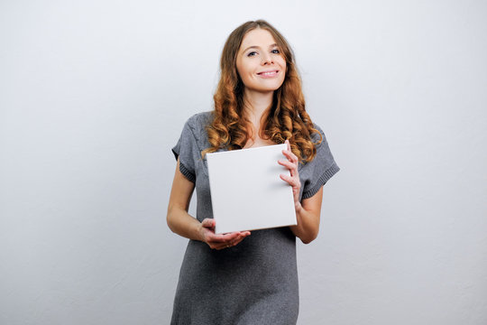 Young woman with blank canvas board smiling on grey background.