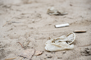 Used dirty latex rubber condom is thrown on sand. Cigarette butts in background. concept of...